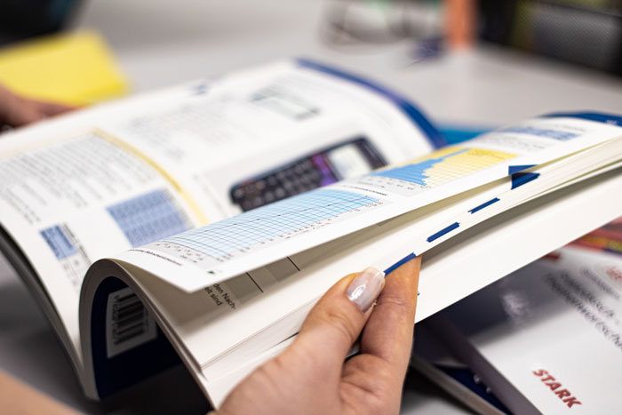 Nahaufnahme einer Person, die in einem Fachbuch blättert.